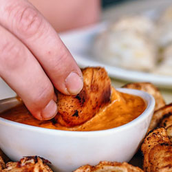 handing dipping food into a sun-dried tomato hummus dip